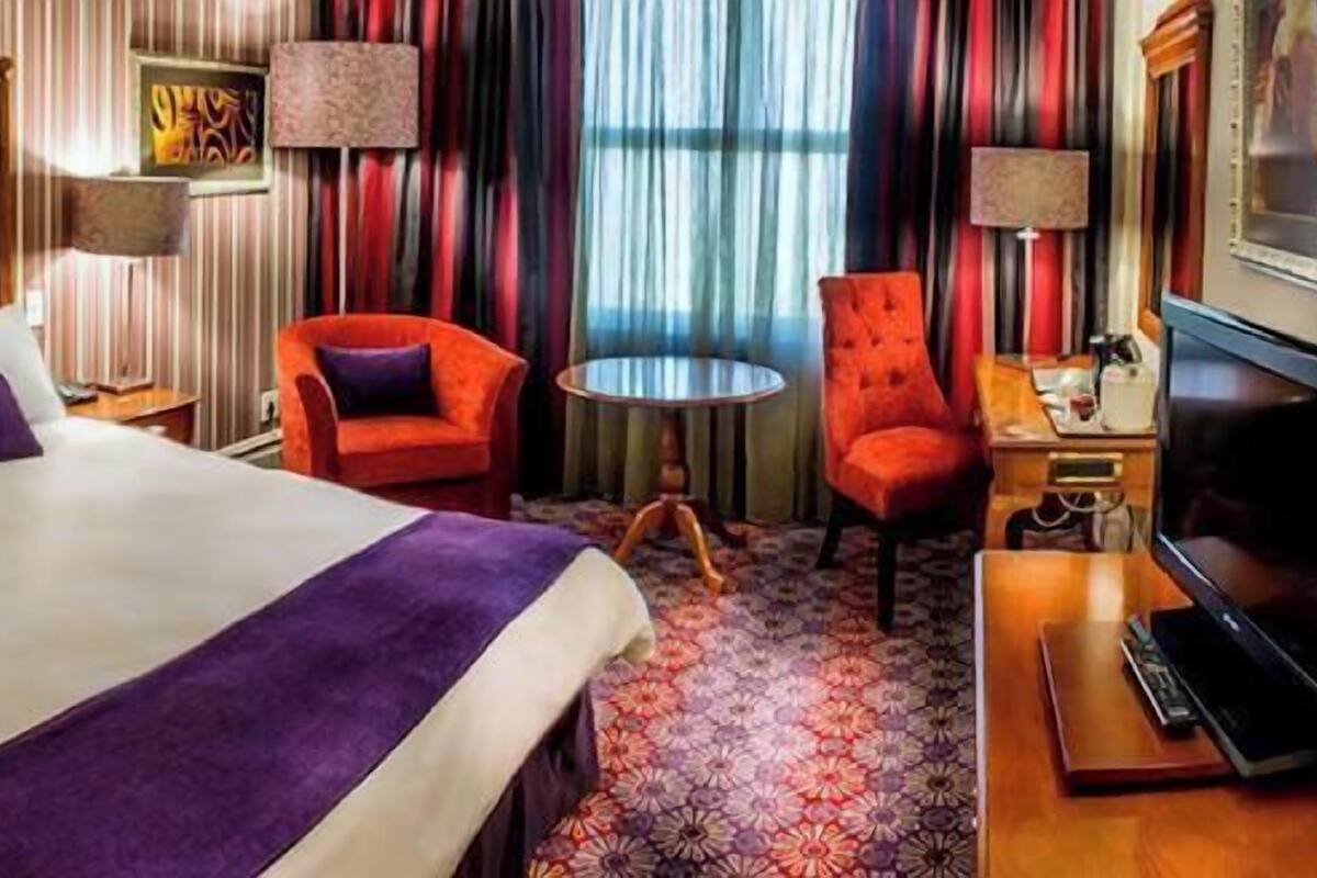 A hotel room with a large bed, a small round table, a red armchair, and a television.