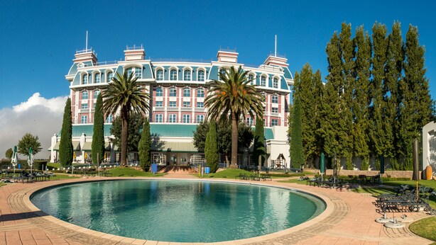 A large hotel with a swimming pool, palm trees, and a clear blue sky. - Peermont Walmont at Graceland, Secunda (Secunda)