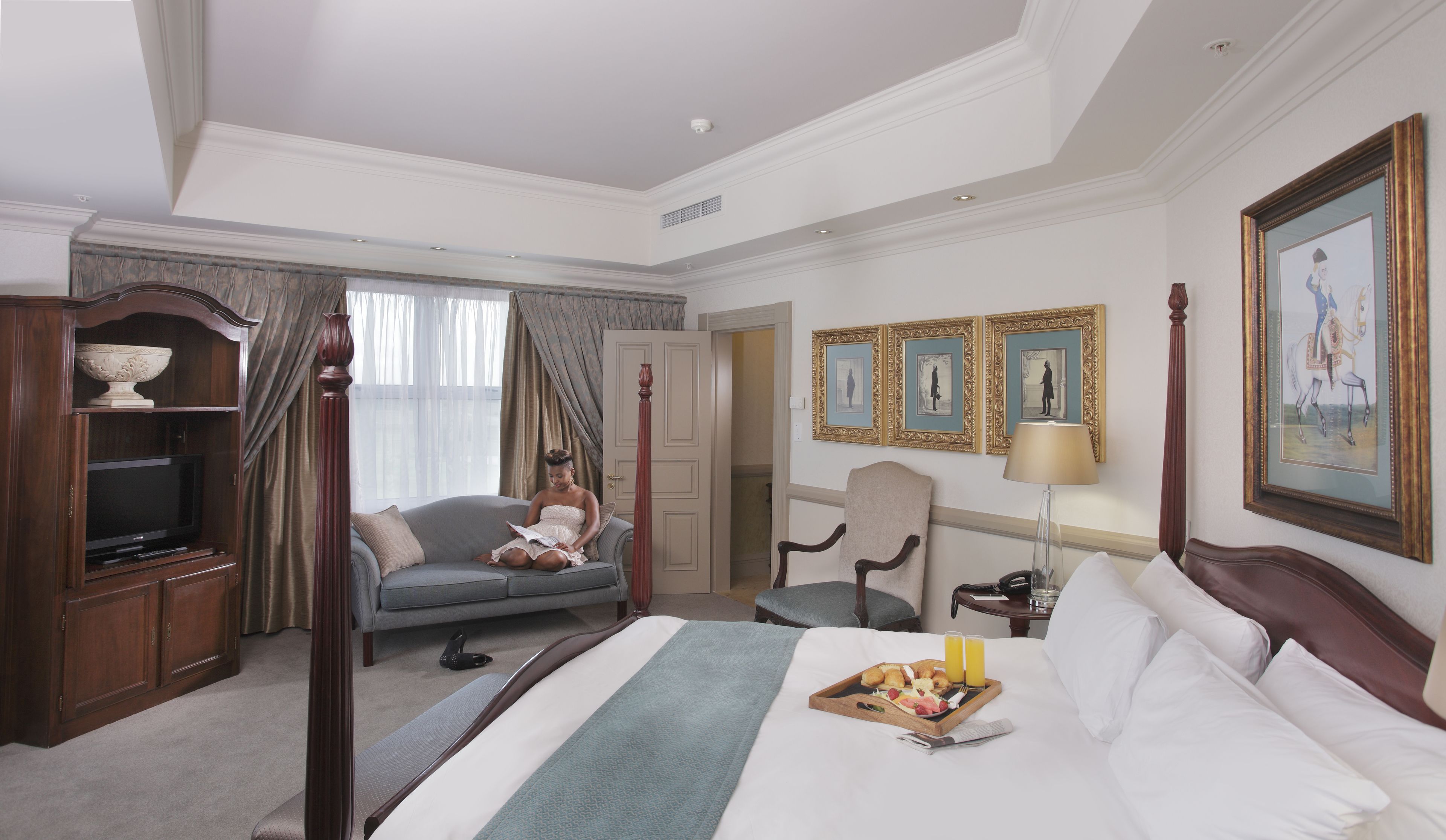 A hotel room with a bed, a television, a seating area, and a dining table with breakfast.