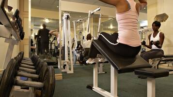 Un gimnasio con equipo de ejercicio, espejos y una persona usando un banco.