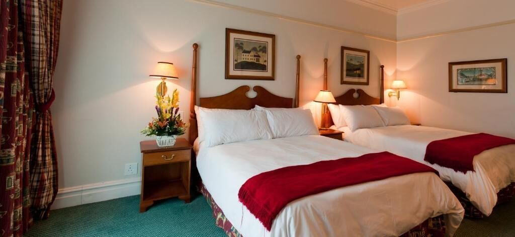 A hotel room with two beds, a nightstand with a lamp, and a floral arrangement.