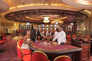 Piso de casino con mesas de blackjack, sillas rojas y máquinas tragamonedas.