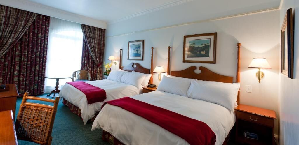 Una habitación de hotel con dos camas, un escritorio, una silla y una lámpara.