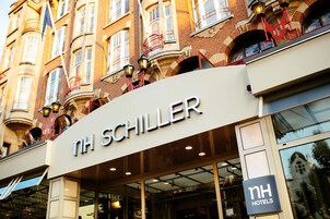 The exterior of NH Schiller hotel with a prominent sign, large windows, and classic architecture.