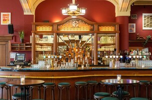 A bar area with a wooden counter, multiple stools, and a variety of bottles and glasses.