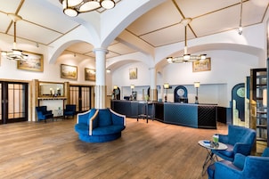 A spacious lobby with a high ceiling, wooden flooring, and blue upholstered seating.