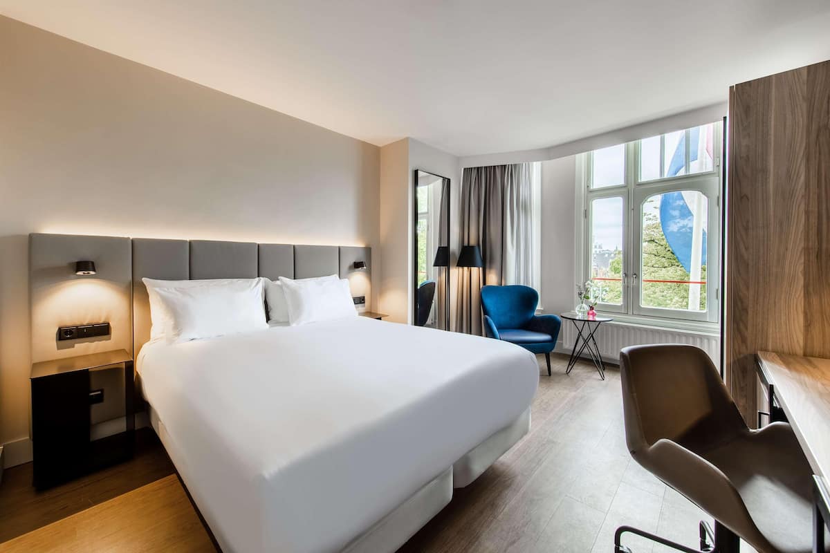 Una habitación de hotel moderna con una cama grande, un escritorio, una silla y una ventana con vistas.