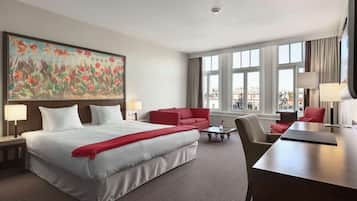 A hotel room with a large bed, a red sofa, a desk, and a large window with a city view.