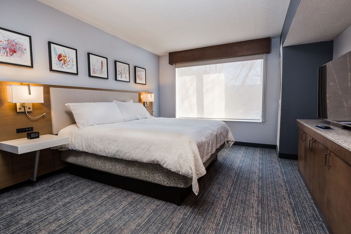 A hotel room with a bed, bedside tables with lamps, a TV, and artwork on the wall.