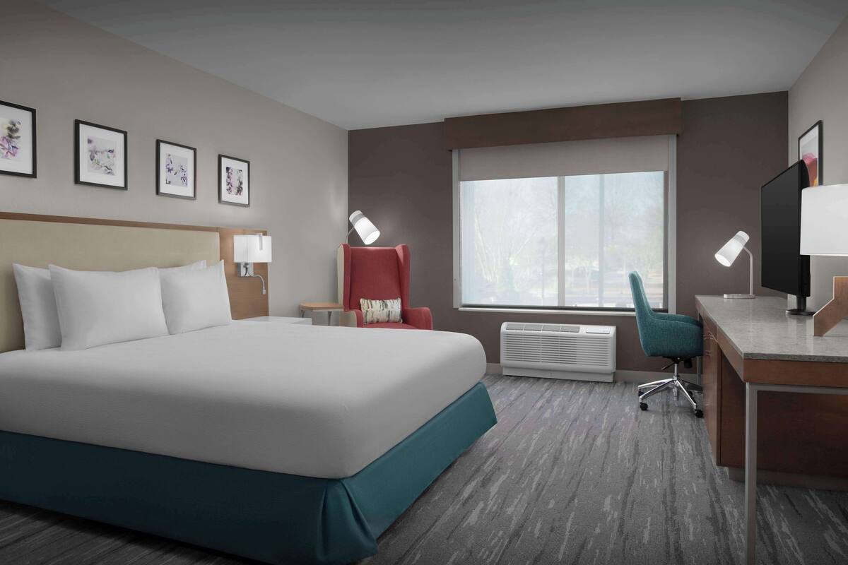 A hotel room with a large bed, a desk, a chair, a TV, and framed pictures on the wall.