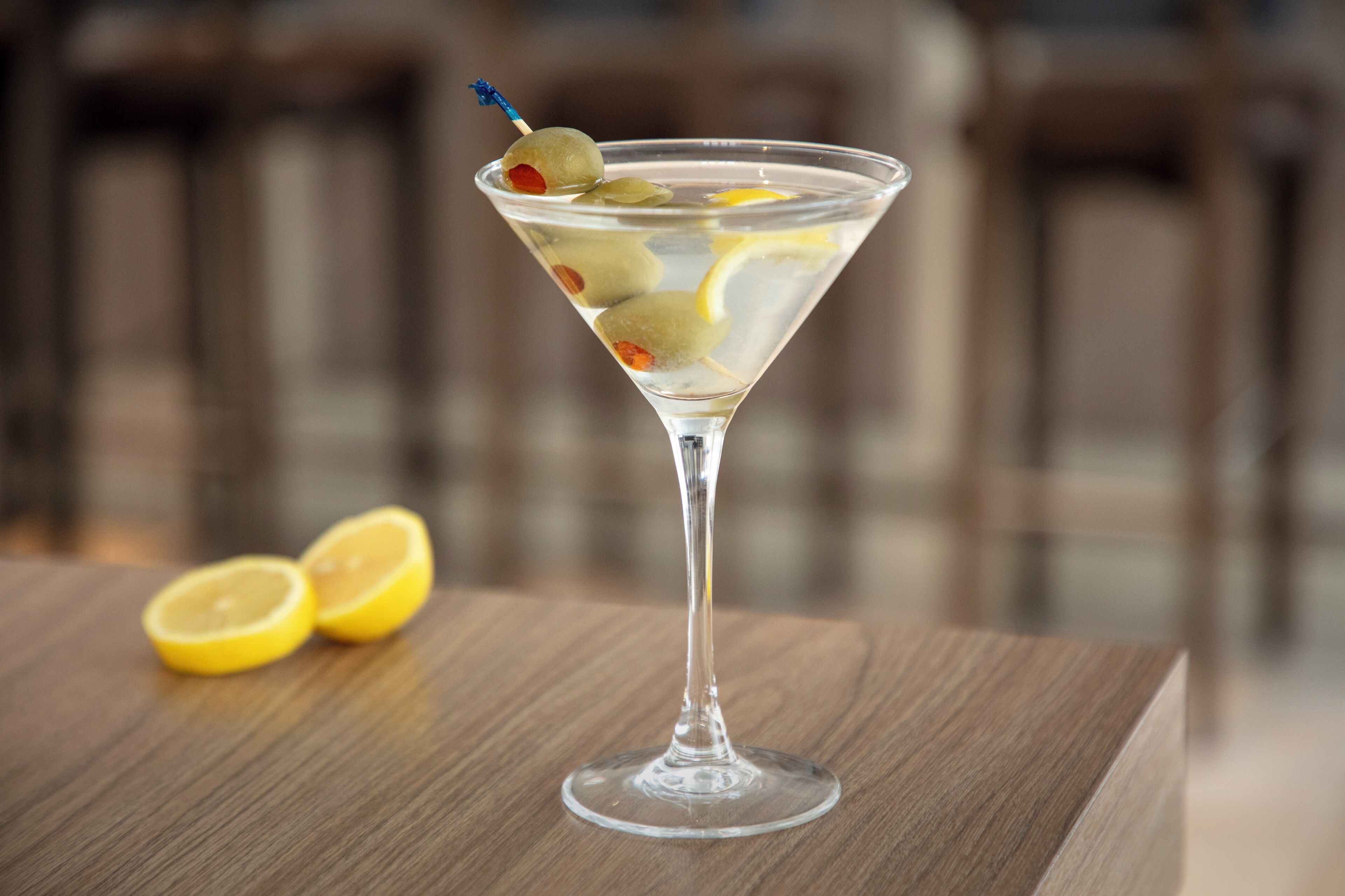 A martini glass with olives and lemon slices on a wooden table.