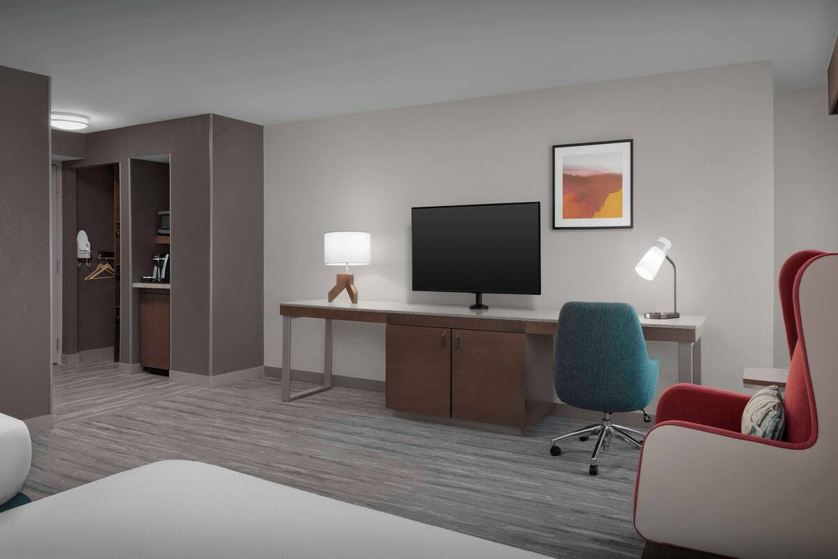 A hotel room with a bed, a desk with a computer, a TV, a chair, and a wardrobe.