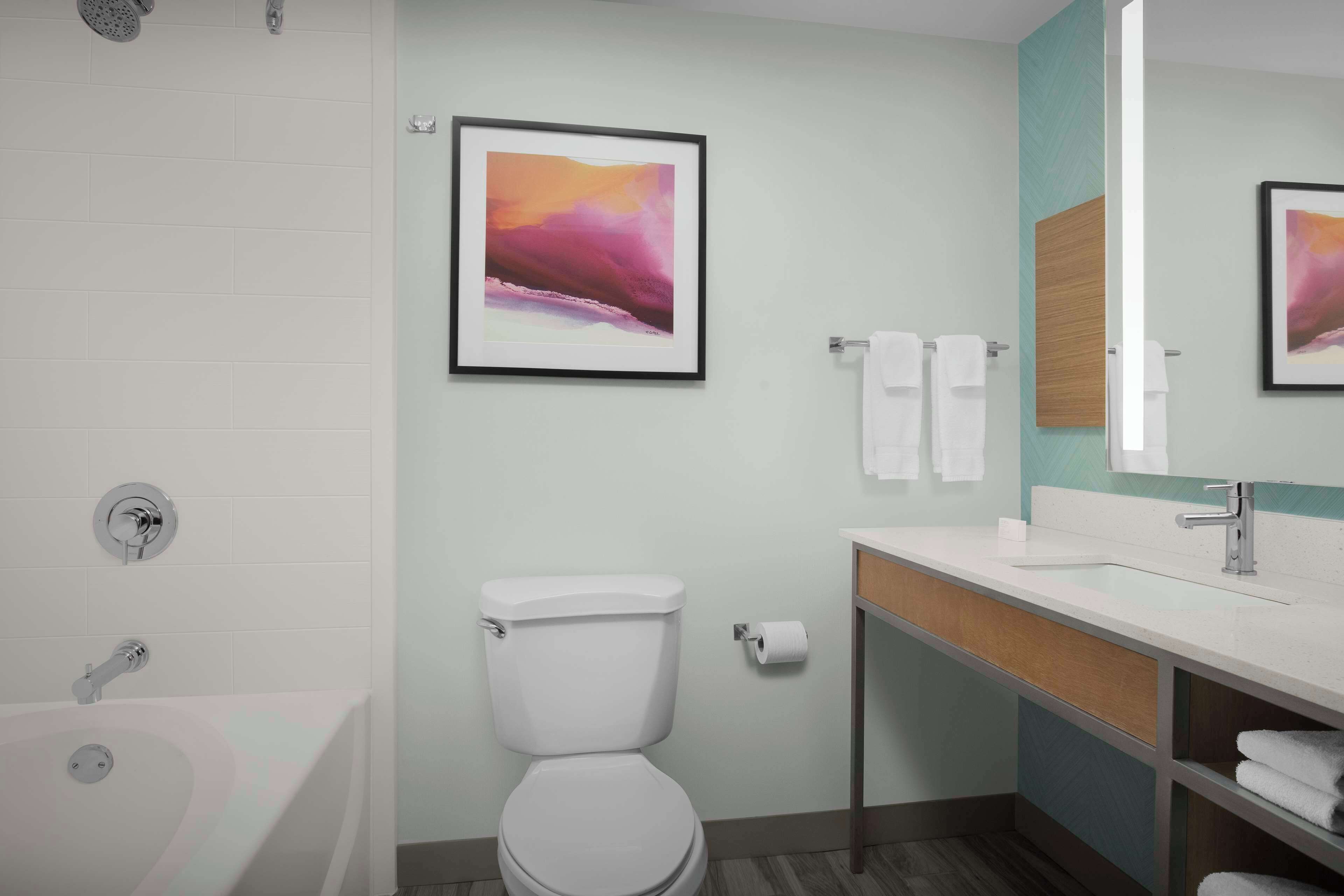Ein modernes Badezimmer mit einer Badewanne, Toilette und Waschbecken. An den Wänden hängen Bilder in Rahmen, und über dem Waschbecken befindet sich ein Spiegel.