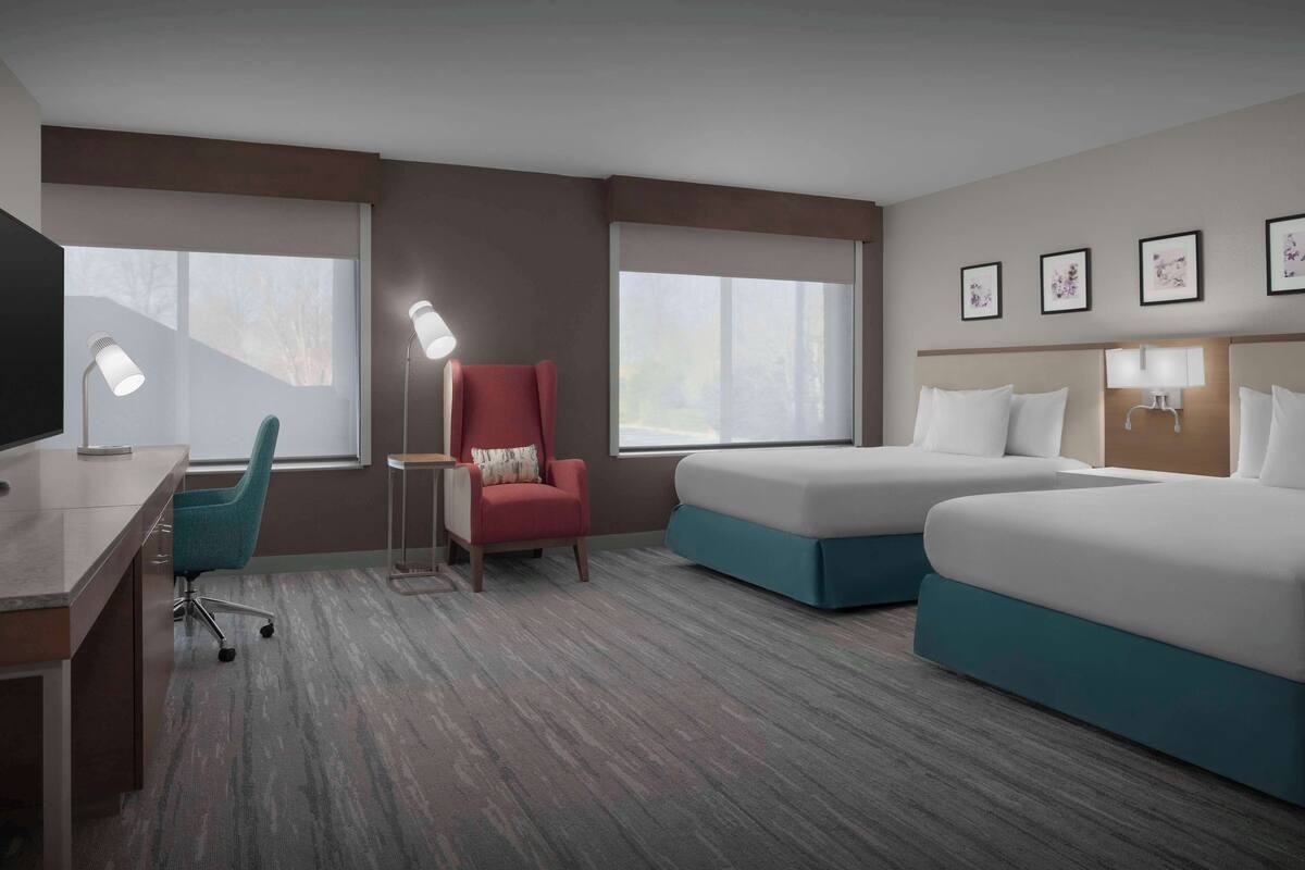 A hotel room with two beds, a desk, a chair, and a TV.