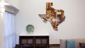 Una sala de estar moderna con una obra de arte de madera en la pared, una consola blanca con un objeto decorativo, y un sofá beige con un cojín azul.