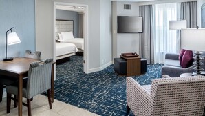 Una habitación de hotel con cama, escritorio con lámpara, televisión, sofá y alfombra estampada.