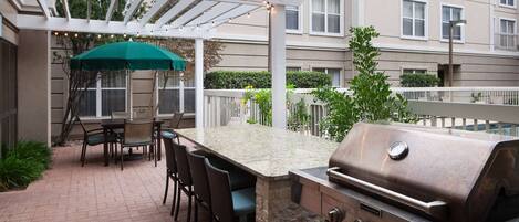 An outdoor patio with a stone grill, bar seating, and a pergola with string lights.