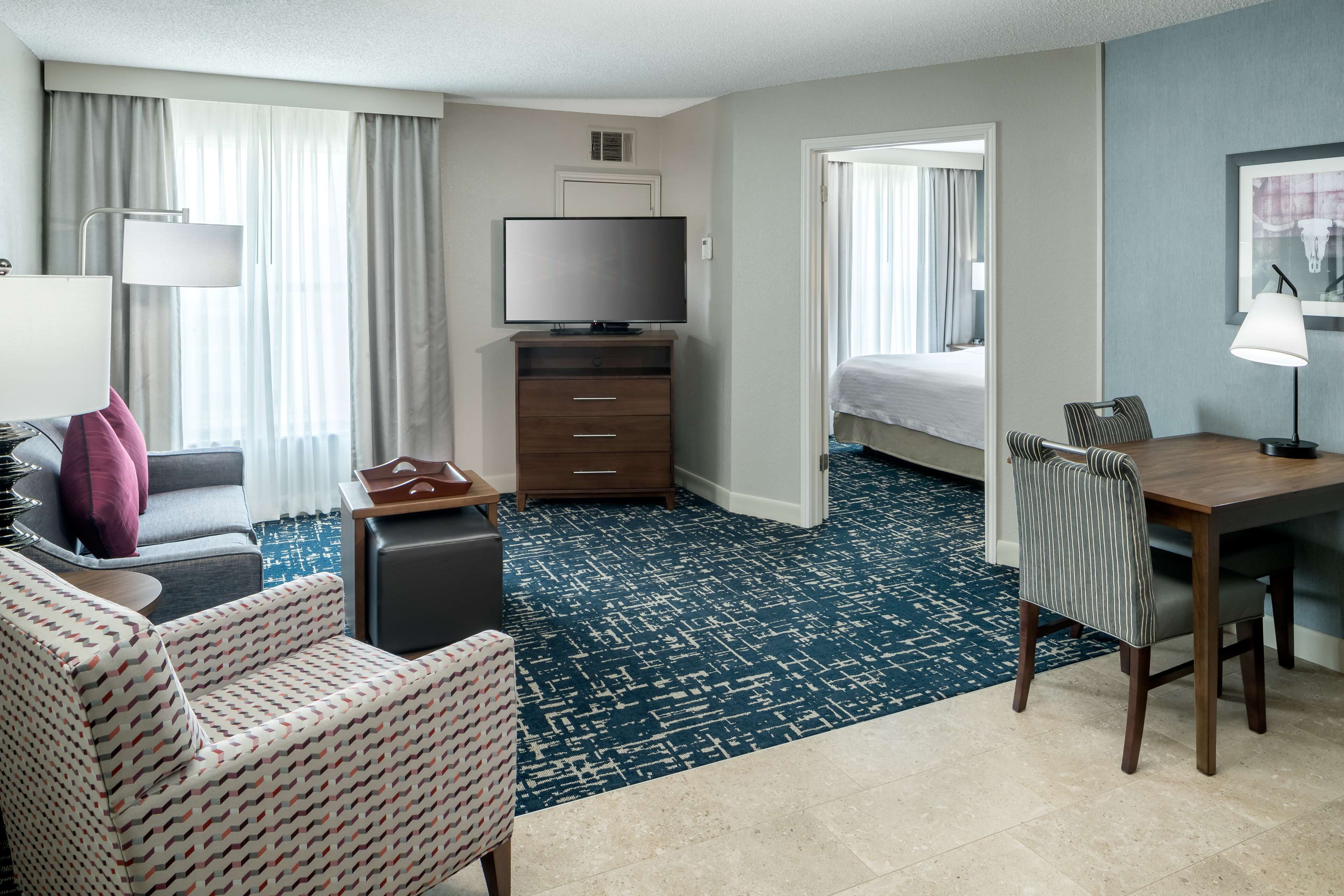 Habitación de hotel con cama, televisión, escritorio, silla, sofá, mesa de centro y alfombra estampada.