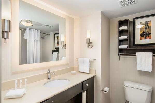 Un baño moderno con un espejo grande, dos lavamanos, ducha y retrete. Hay toallas y artículos de aseo en la encimera.
