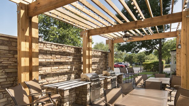 Eine Terrasse im Freien mit Steinmauern, einer Holz-Pergola und Grillanlagen.