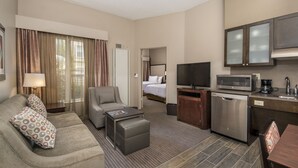 Ein Hotelzimmer mit einer Couch, einem Sessel, einem Couchtisch, einem Fernseher, einer Küchenzeile und einem Bett.