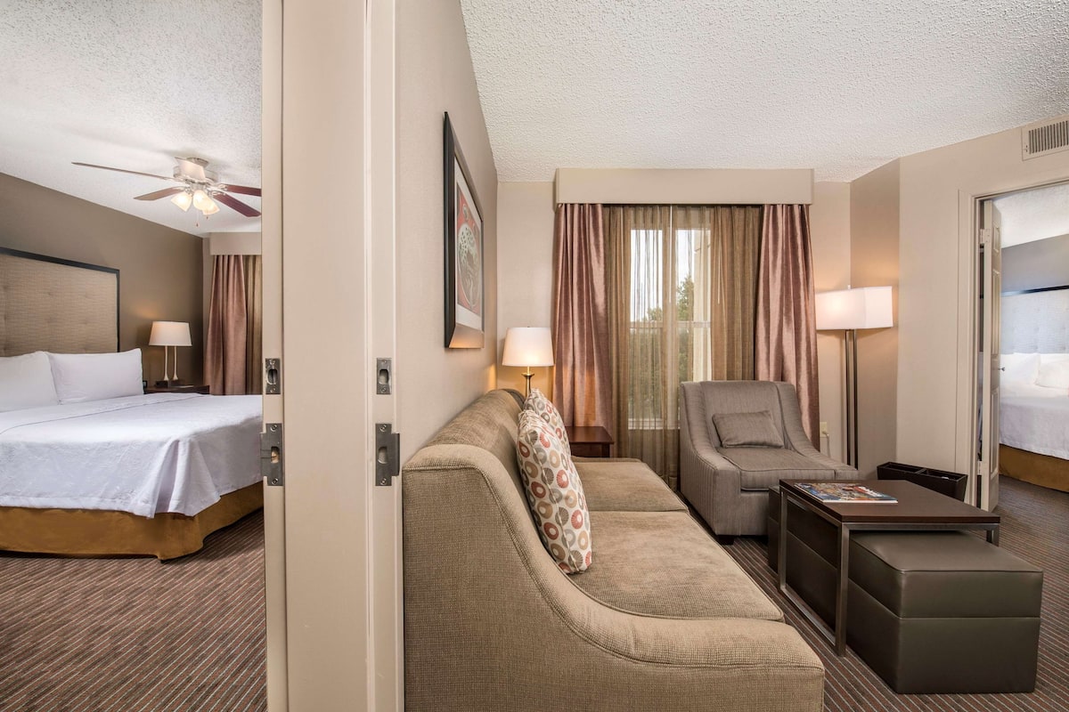 A hotel room with a bed, a sofa, a chair, a small table, and a ceiling fan.