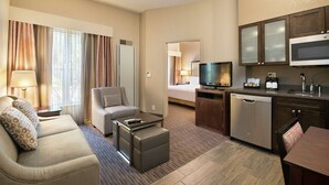 Ein Hotelzimmer mit Wohnbereich, einer Couch, einem Couchtisch, einem Fernseher und einer Küchenzeile inklusive Mikrowelle und Geschirrspüler.