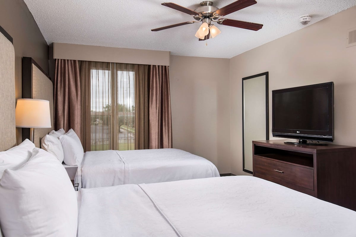 A hotel room with two beds, a ceiling fan, a TV, and a window with curtains.