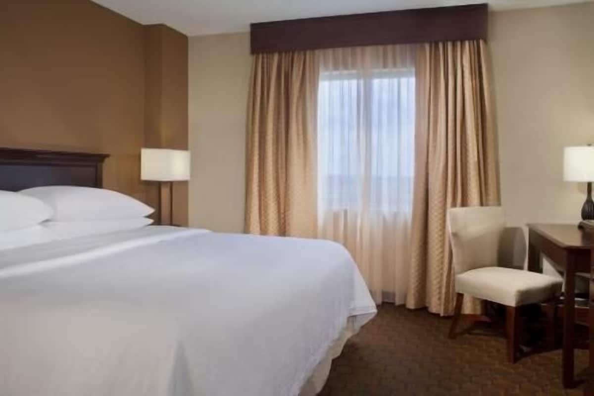 A hotel room with a large bed, a desk with a chair, and a window with curtains.