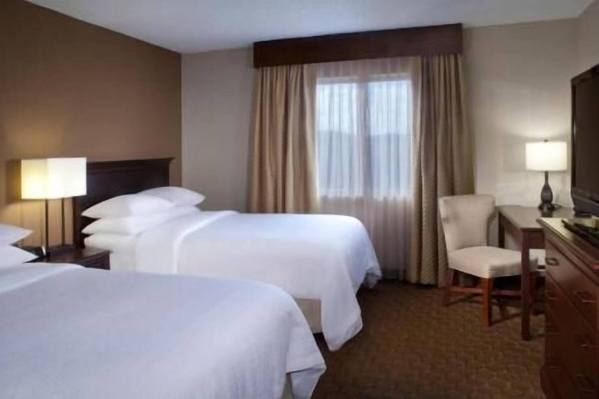 Una habitación de hotel con dos camas, un escritorio, una silla y un televisor.
