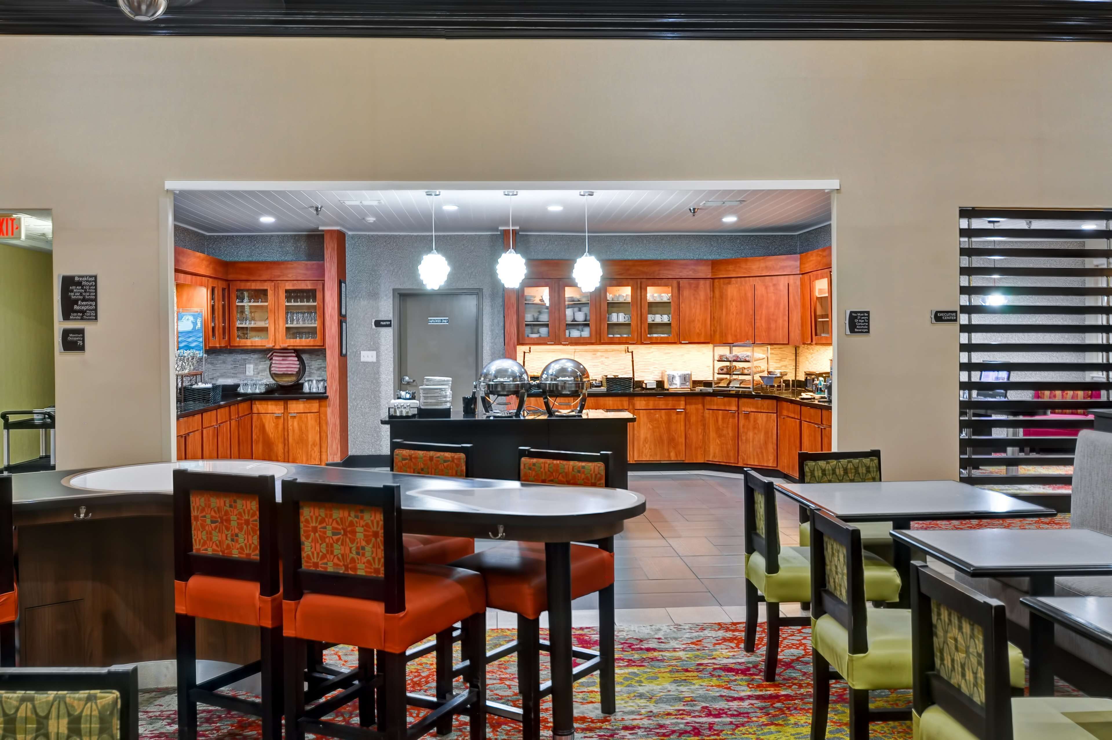 A hotel lobby with a central dining area, a kitchen, and a seating area with tables and chairs.