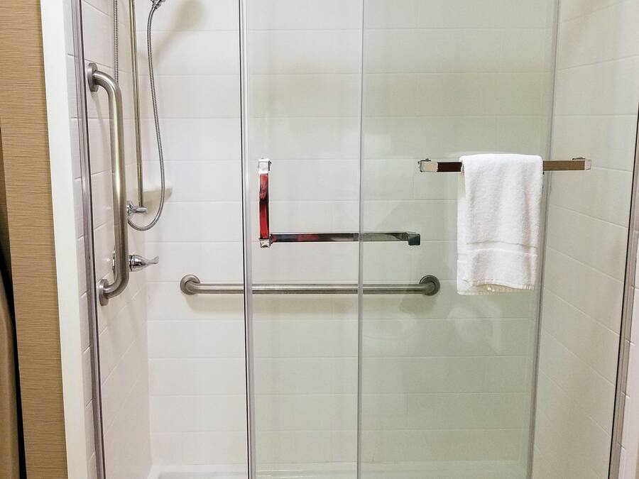 A glass-enclosed shower stall with a handrail, a towel rack, and a glass door.