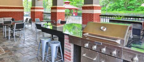 An outdoor patio with a grill, seating, and a view of the park.