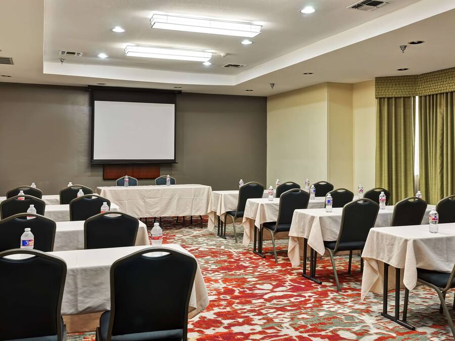 Un salón de conferencias con varias mesas y sillas, una pantalla de proyector y piso alfombrado.
