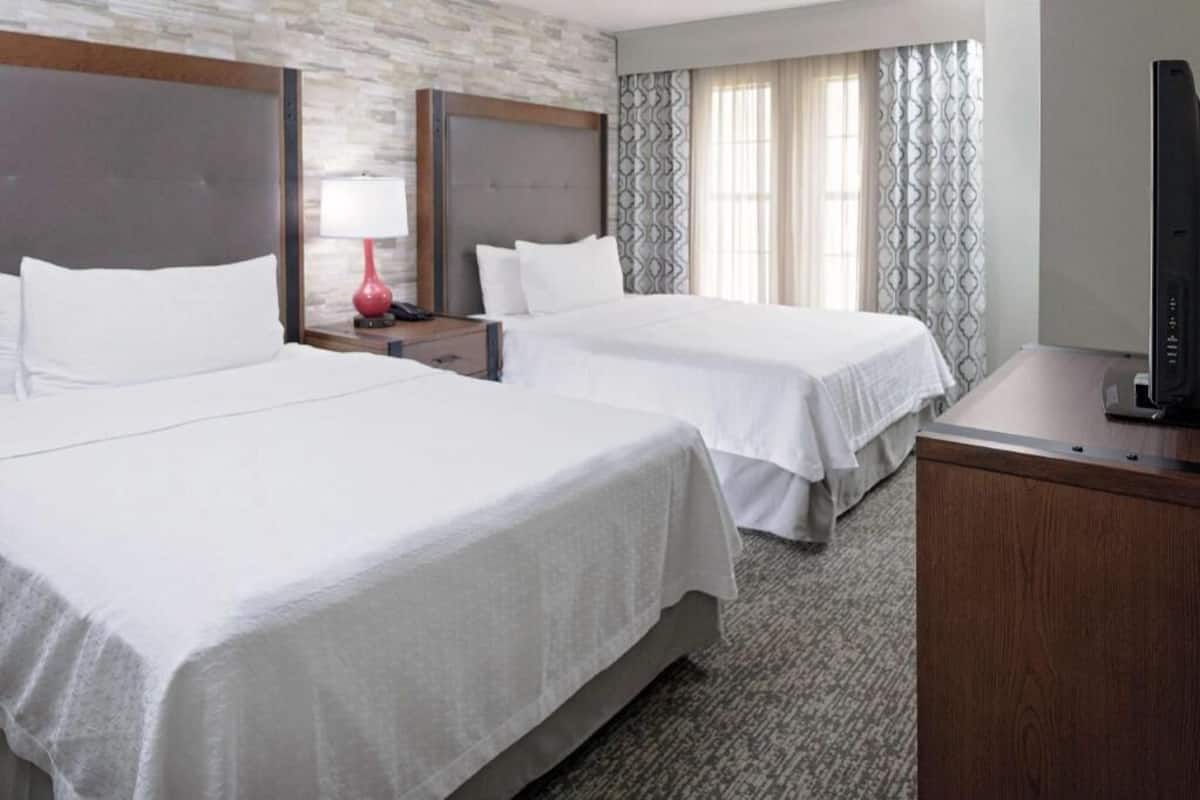 Habitación de hotel con dos camas, un escritorio, televisor y ventana con cortinas.