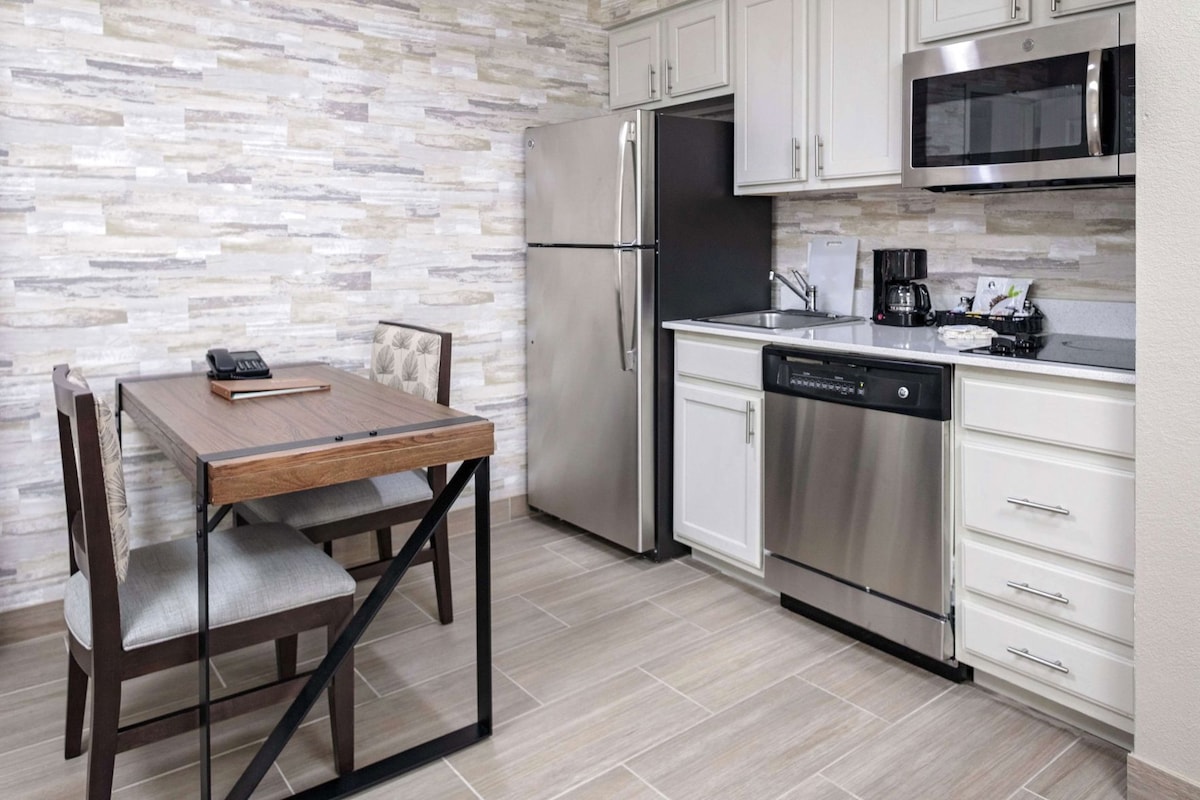 A kitchen with a wooden table, chairs, a refrigerator, a dishwasher, and a microwave.