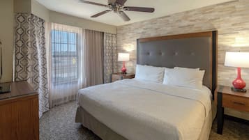 Quarto de hotel com uma cama grande, um ventilador de teto, uma mesa de cabeceira de madeira, um abajur vermelho e cortina estampada.
