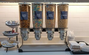 A breakfast bar with four dispensers labeled Raisin Bran, Fru Loops, Lucky Charms, and Cheerios.