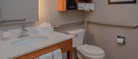 A modern bathroom with a sink, toilet, and hand dryer. There are towels and a tissue box on the counter.