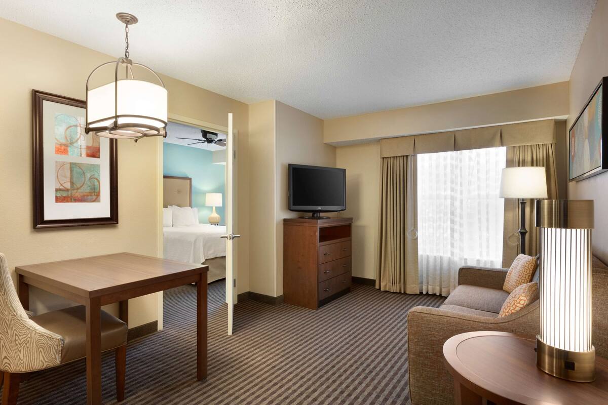 A hotel room with a bed, a TV, a desk, a chair, a sofa, and a lamp.