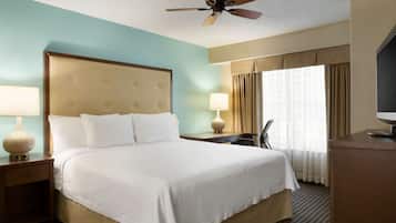 Ein Hotelzimmer mit einem großen Bett, einem Schreibtisch, einem Sessel, einem Fernseher und einem Deckenventilator.