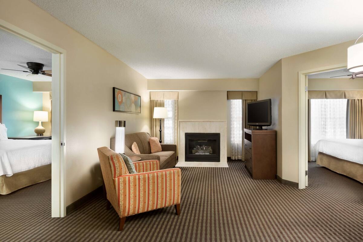 A hotel room with a bed, a sofa, a chair, a television, a fireplace, and a door leading to another room.