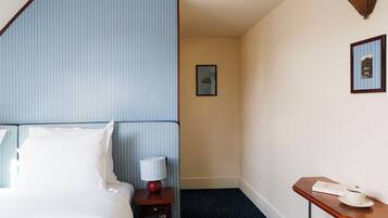 A hotel room with a bed, a bedside table with a lamp, a small table with a cup and a menu, and a framed picture on the wall.