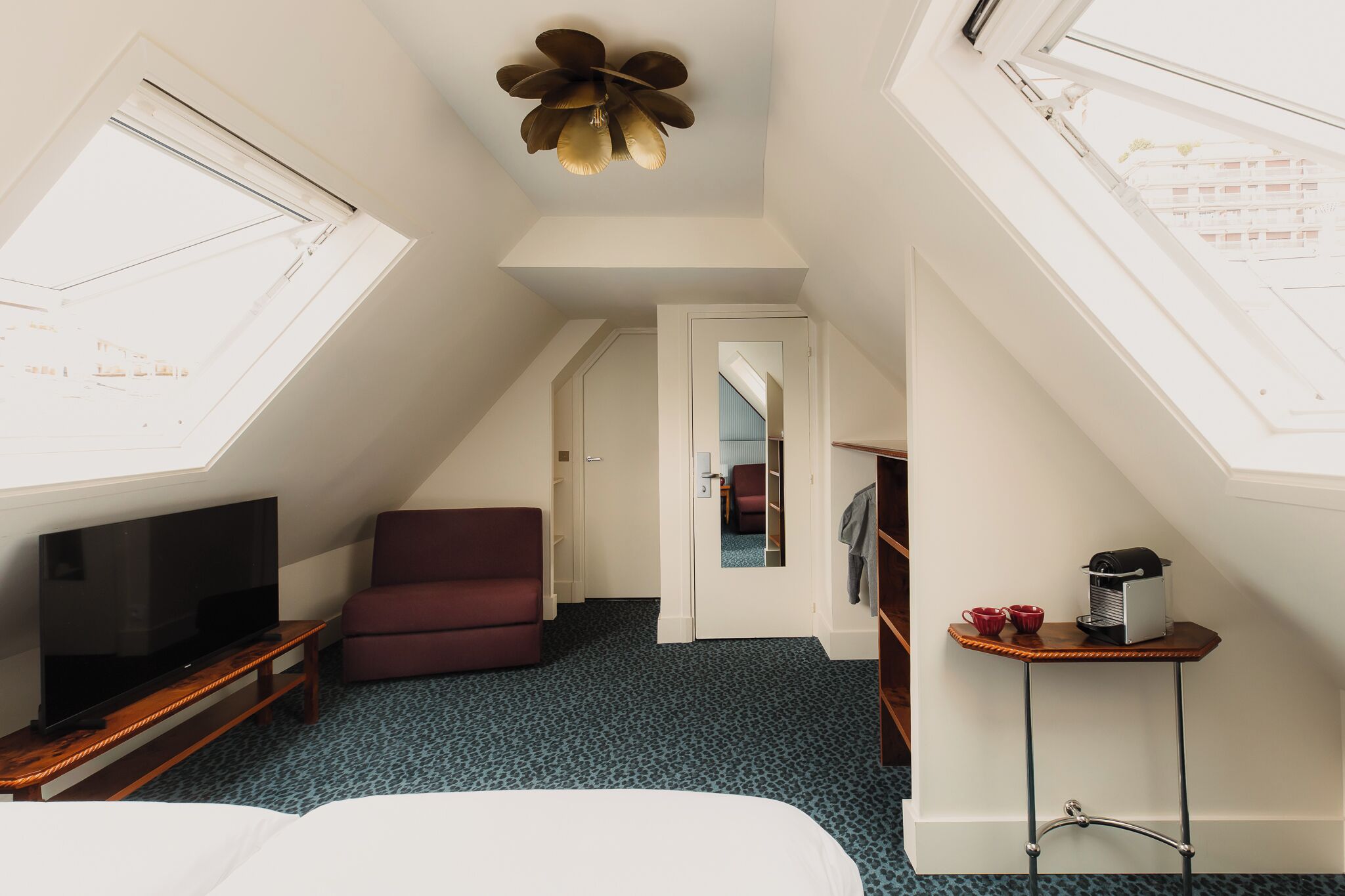 A hotel room with a TV, a red chair, a small table with cups, and a ceiling fan.
