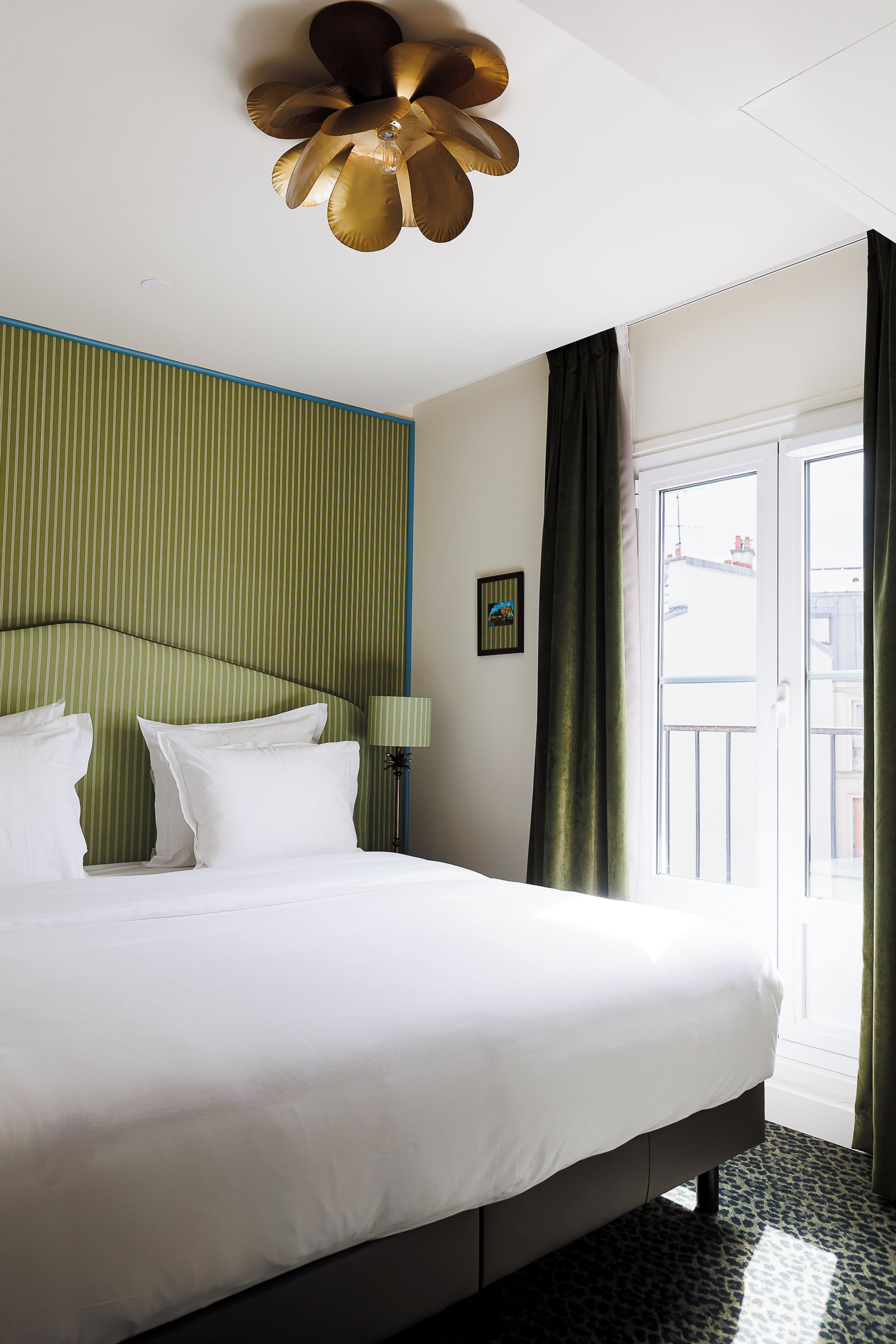 A hotel room with a bed, a ceiling fan, a window with curtains, and a wall with a striped pattern.