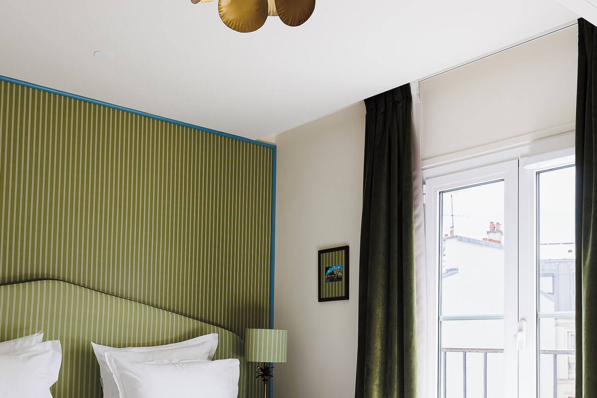 A hotel room with a bed, a ceiling fan, a window with curtains, and a wall with a striped pattern.