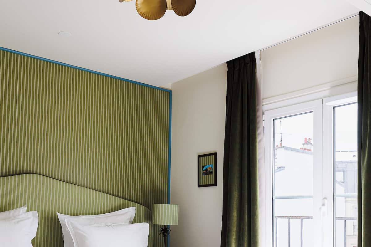 Une chambre d’hôtel avec un lit, un ventilateur de plafond, une fenêtre avec des rideaux et un mur à motifs rayés.
