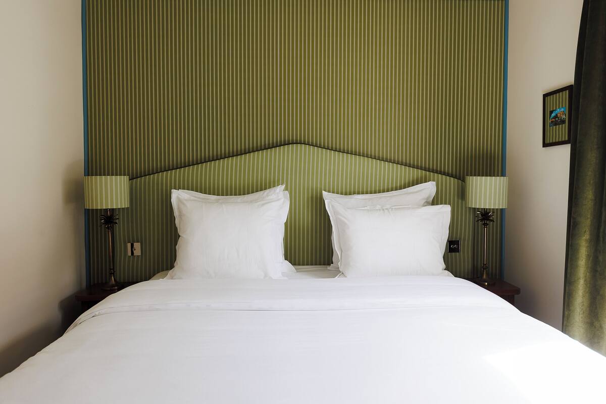A neatly made bed with white linens, two bedside lamps, and a green-striped headboard.