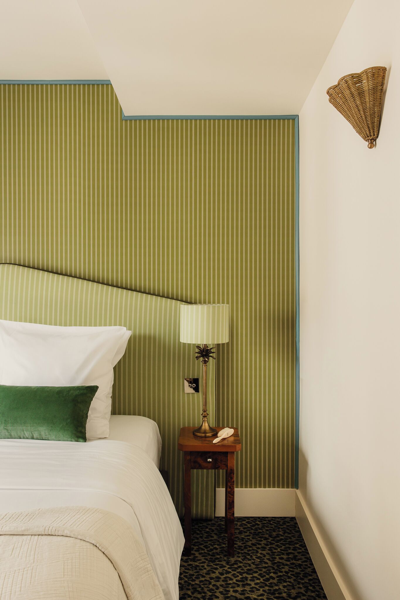 Una camera d'albergo con un letto, un comodino con una lampada e una parete a righe verticali.