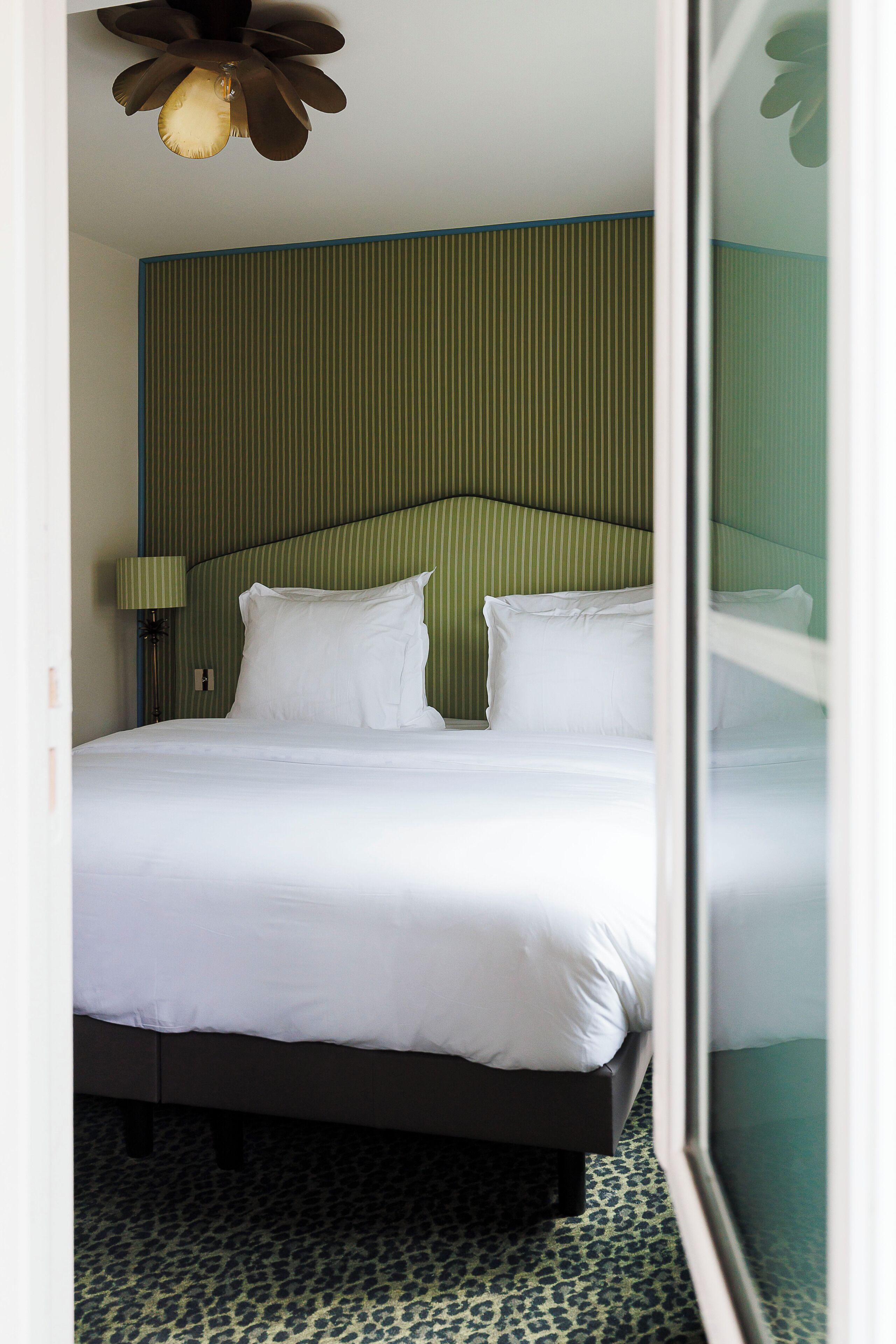 A hotel room with a bed, a headboard, a lamp, and a patterned carpet.